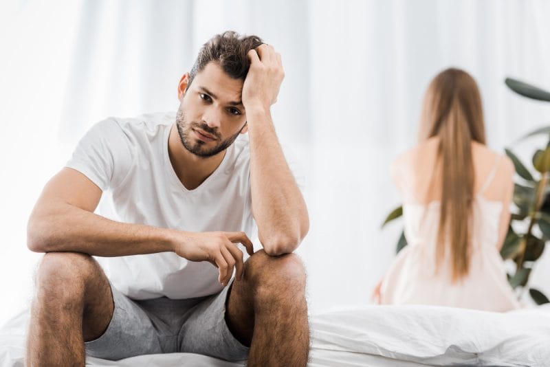 upset man with sexual problems sitting on bed with girlfriend