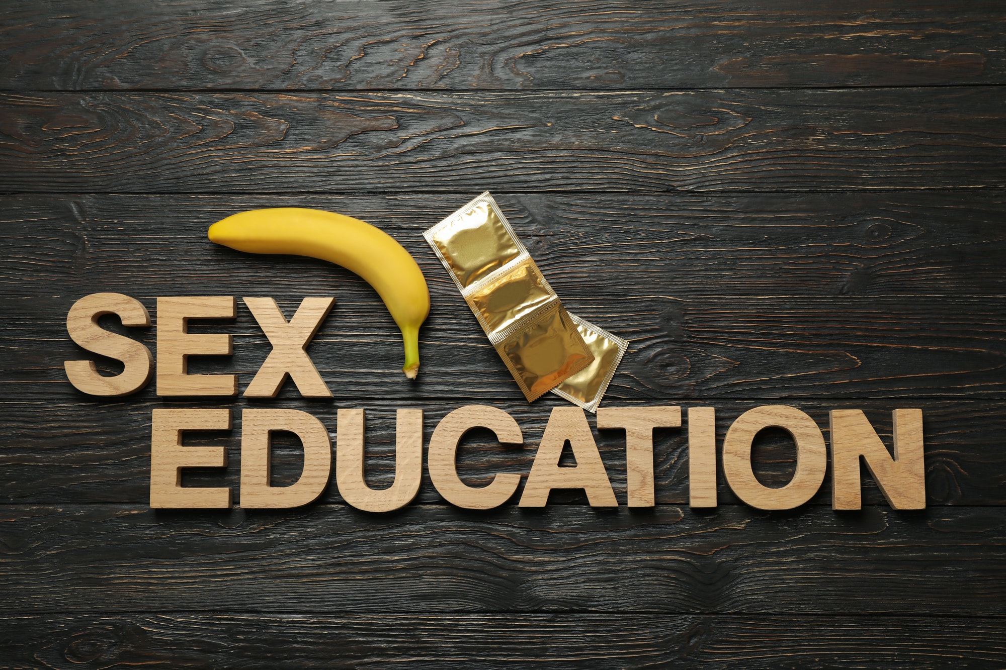 Words Sex Education, banana and condoms on wooden background